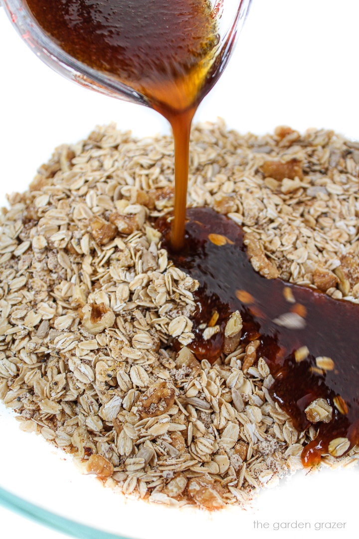 Liquid ingredients being poured into bowl of dry granola ingredients