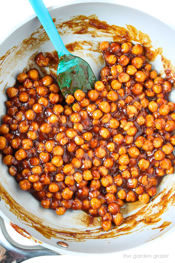 Overhead view of chickpeas simmering in BBQ sauce in a small skillet with spatula