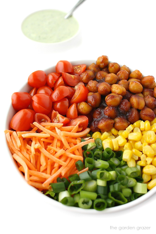 Garbanzo beans, carrots, tomato, sweet corn, and green onion ingredients in a white bowl