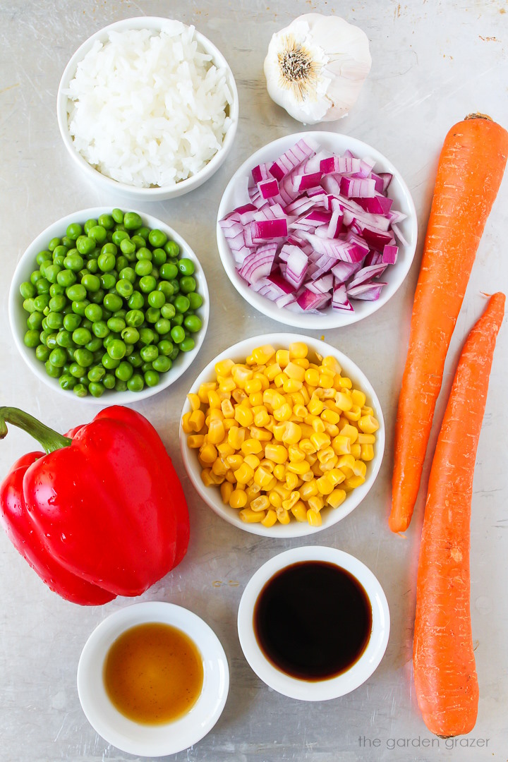 Carrots, bell pepper, red onion, sweet corn, peas, garlic, and tamari ingredients laid out on a metal tray