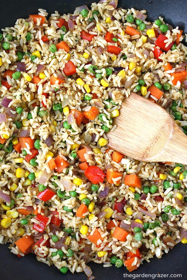 Cooking vegetable fried rice in a skillet with wooden spoon