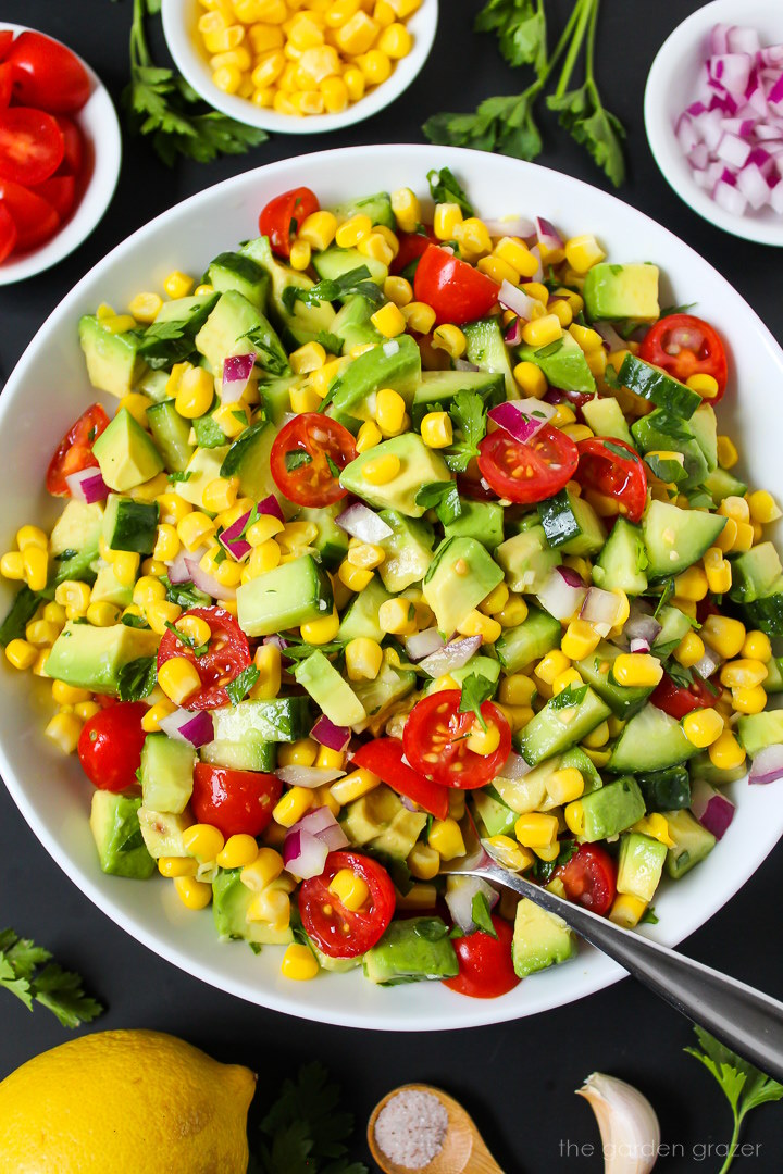 Overhead view of avocado corn salad in a white serving bowl with spoon