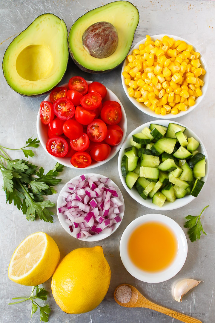 Sweet corn, tomato, parsley, red onion, lemon, vinegar, garlic, and salt ingredients laid out on a metal tray