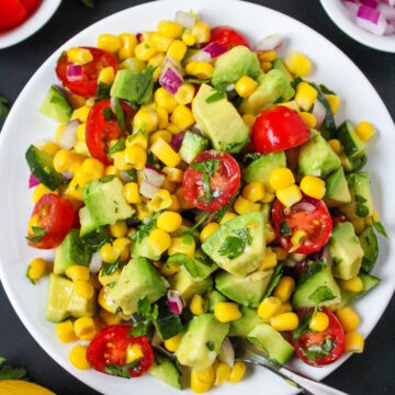 Avocado corn salad on a white plate with serving spoon