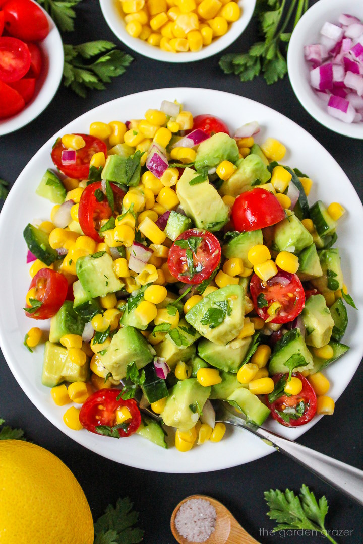 Avocado corn salad on a white plate with serving spoon