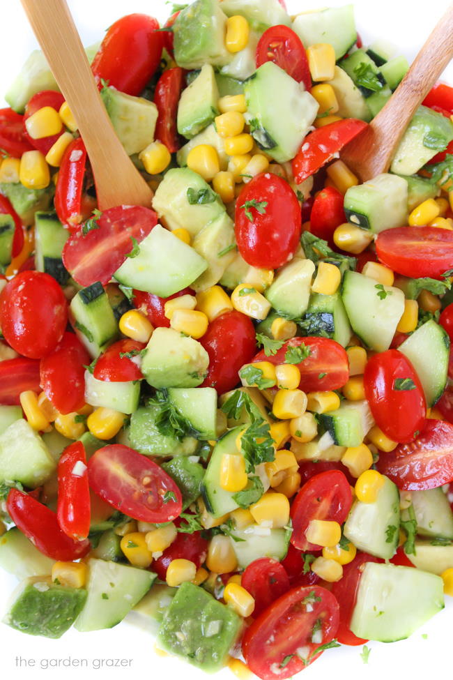 Bowl of vegan avocado summer salad with cucumber, tomato, corn, and herbs