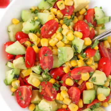 Summer avocado salad with tomato, cucumber, and corn in a bowl with spoon