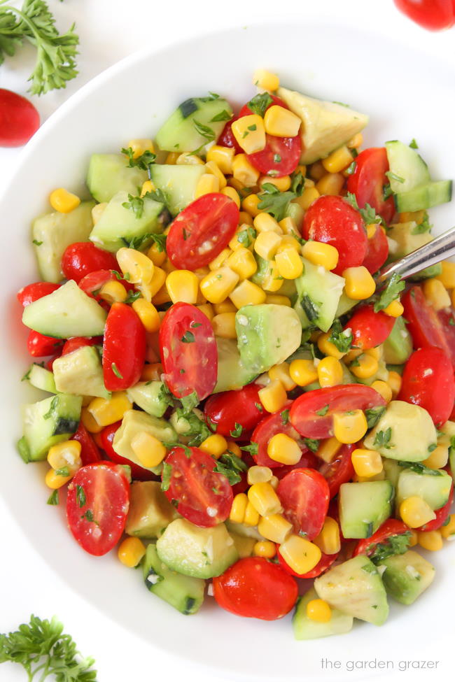 Summer avocado salad with tomato, cucumber, and corn in a bowl with spoon