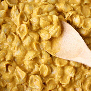 Cooked vegan mac and cashew cheese in a large skillet with wooden spoon