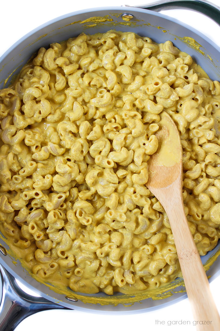 Cooked vegan mac and cashew cheese in a large skillet with wooden spoon