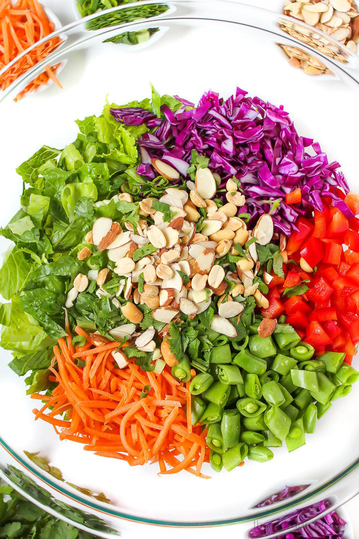 Overhead view of preparing salad ingredients in a large glass bowl before mixing together