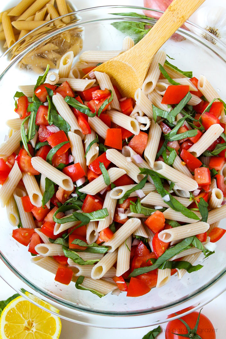 Overhead view of fresh tomato pasta with lemon and basil mixed together with wooden stirring spoon
