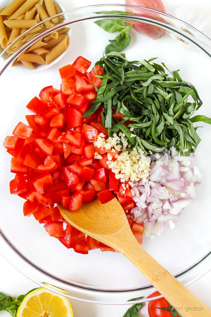 Overhead view of preparing fresh tomato pasta in a large glass bowl before mixing together