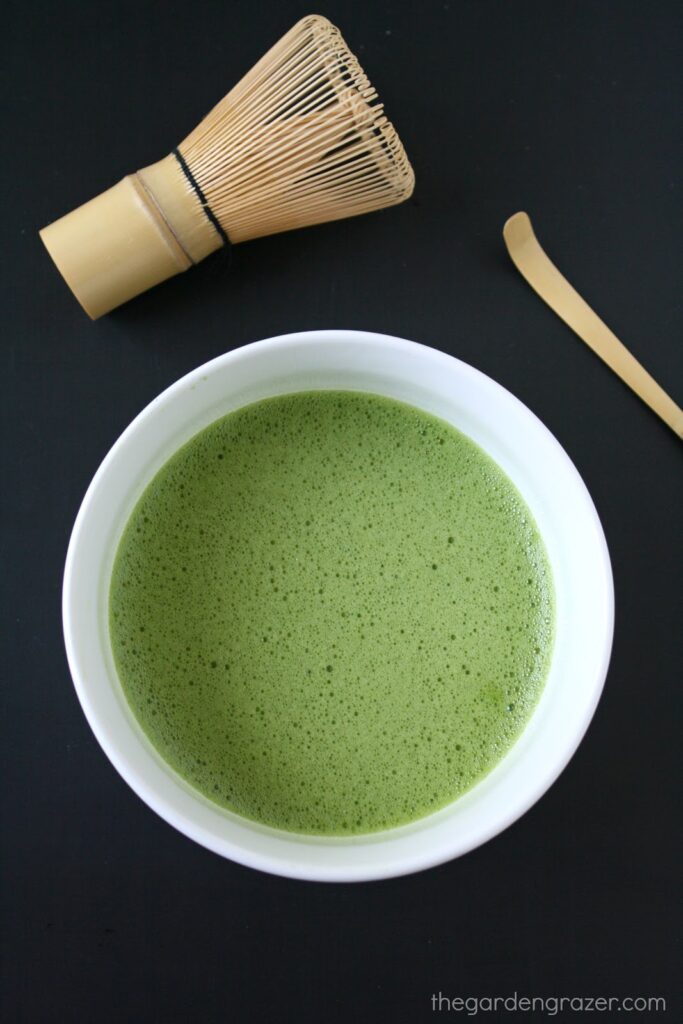 Bowl of whisked matcha green tea with bamboo whisk and scoop