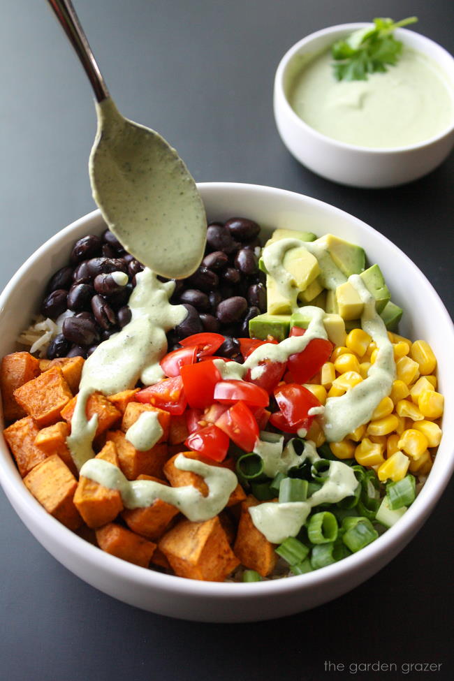 Cashew cream being drizzled over a black bean potato bowl with corn