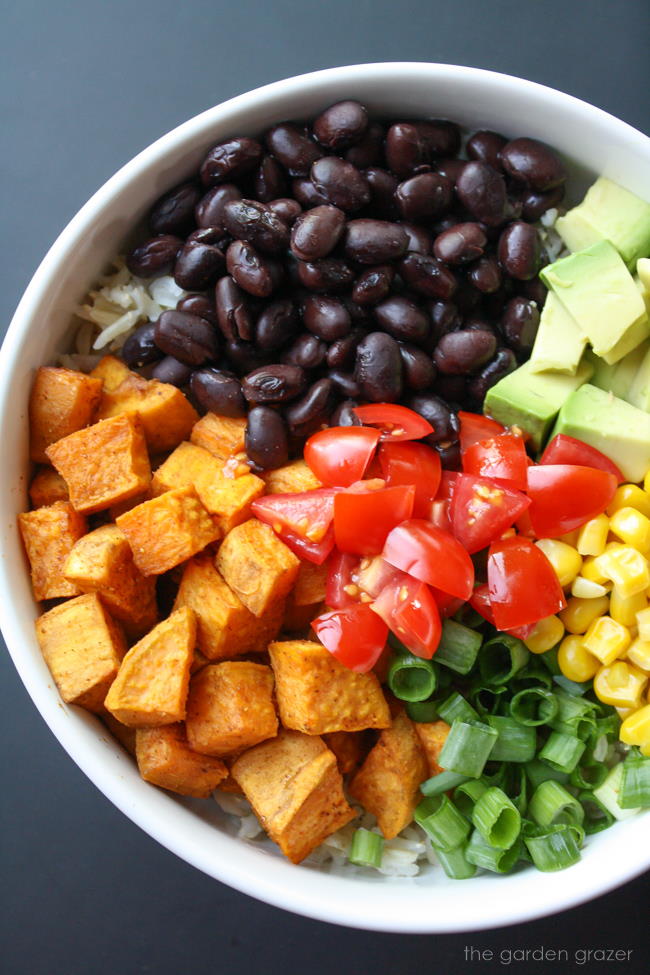 Chopped ingredients on top of brown rice in a white bowl