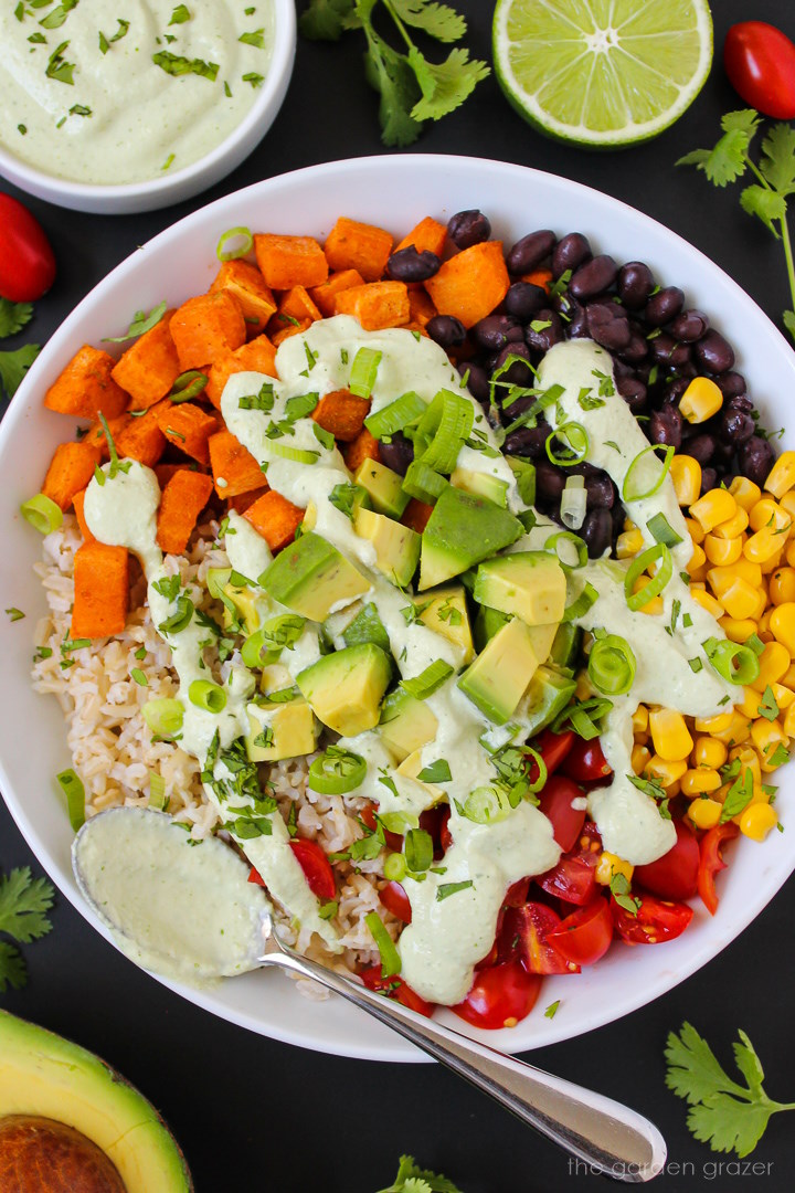 Close up view of a sweet potato bowl with brown rice, black beans, veggies, and a cilantro lime cashew sauce