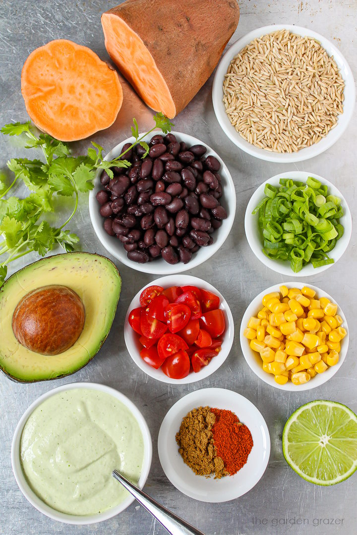 Black beans, avocado, tomato, green onions, sweet corn, brown rice, and spice ingredients laid out on a metal tray