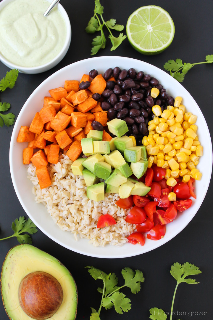 Overhead view of preparing sweet potato black bean rice bowl with creamy cilantro sauce on the side