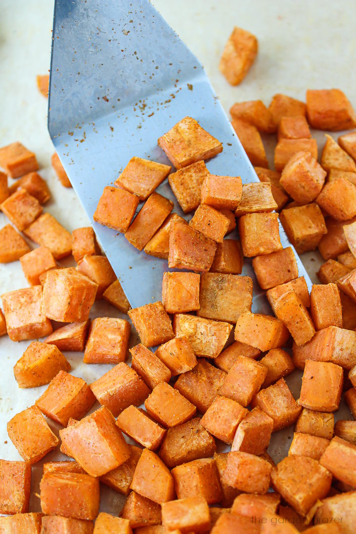 A metal spatula lifting up diced sweet potatoes after roasting in the oven