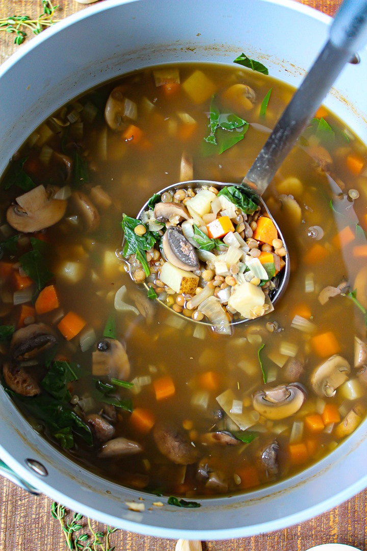 A ladle lifting up Rustic Lentil Potato Soup cooking in a large pot