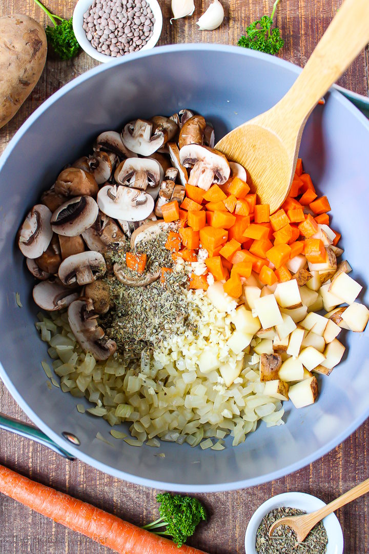 Overhead view of preparing soup in a large stockpot with wooden stirring spoon