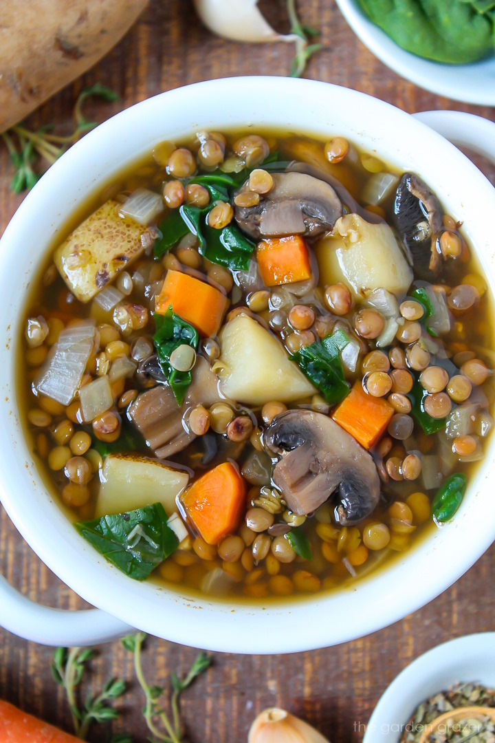 Close up view of rustic lentil potato soup with mushrooms in a white serving bowl