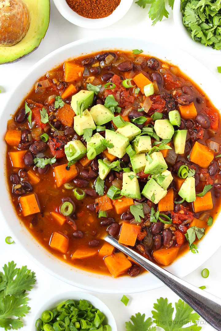 Overhead view of sweet potato black bean chili in a white bowl topped with avocado and cilantro