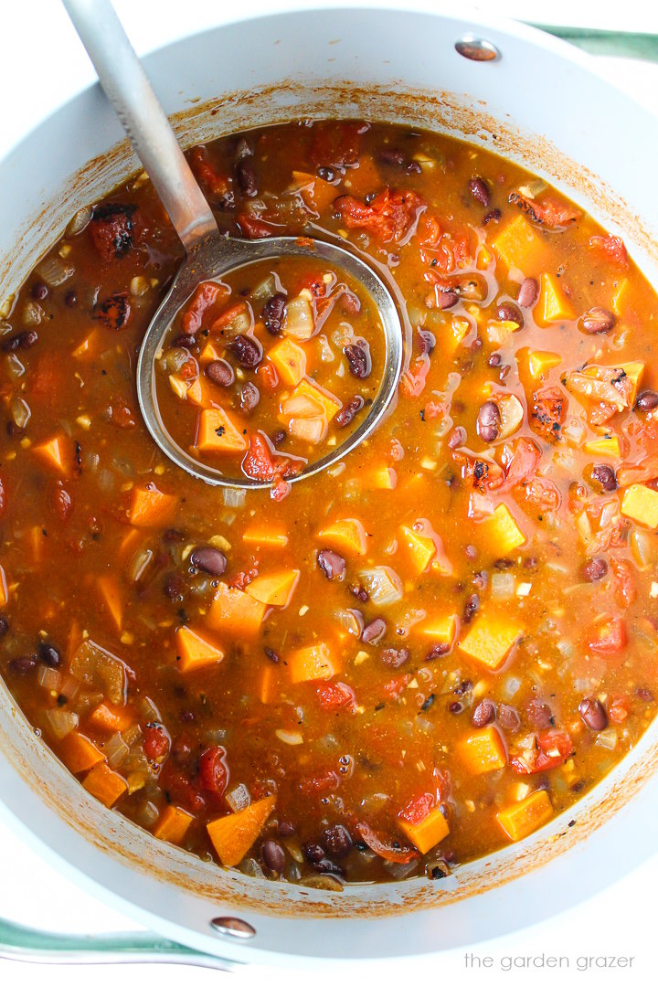 Sweet potato black bean chili cooking in a large pot with metal ladle