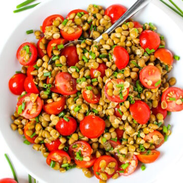 Lentil tomato salad in a white bowl with fresh chives and vinegar dressing