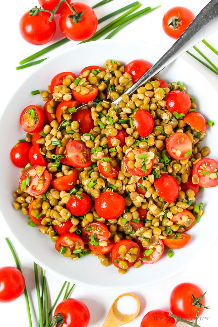 Lentil tomato salad in a white bowl with fresh chives and vinegar dressing