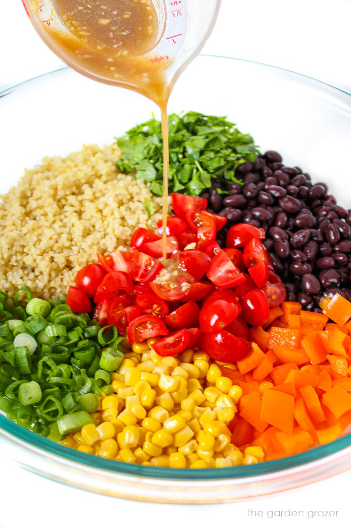 Cumin lime dressing being poured over a quinoa salad before mixing together