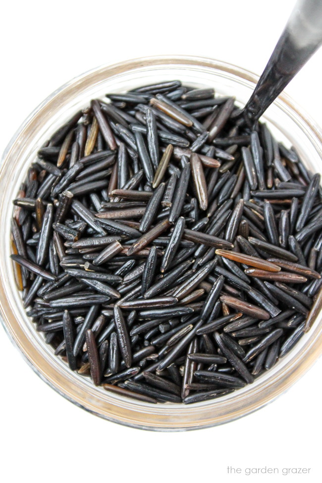 Uncooked raw wild rice in a small glass jar with spoon