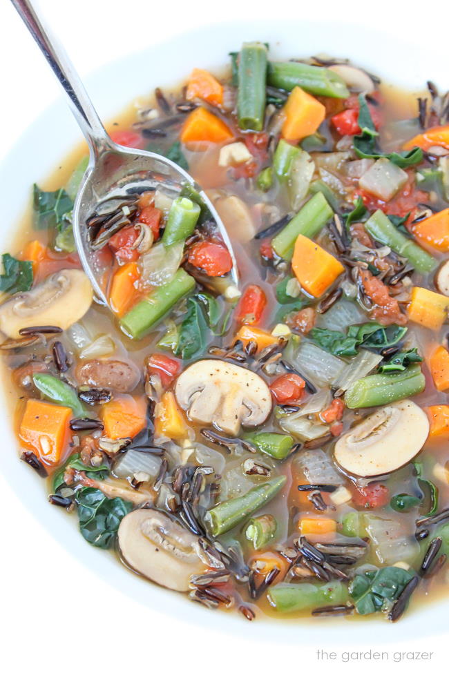 Wild rice vegetable soup in a white bowl with spoon