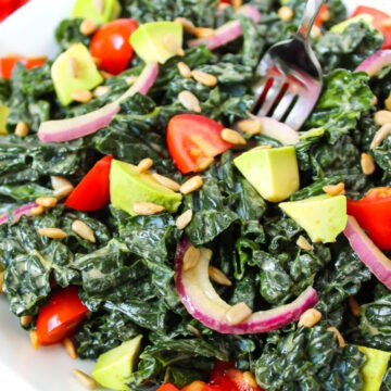 A fork piercing Marinated Kale Salad served on a white plate with avocado and tomato