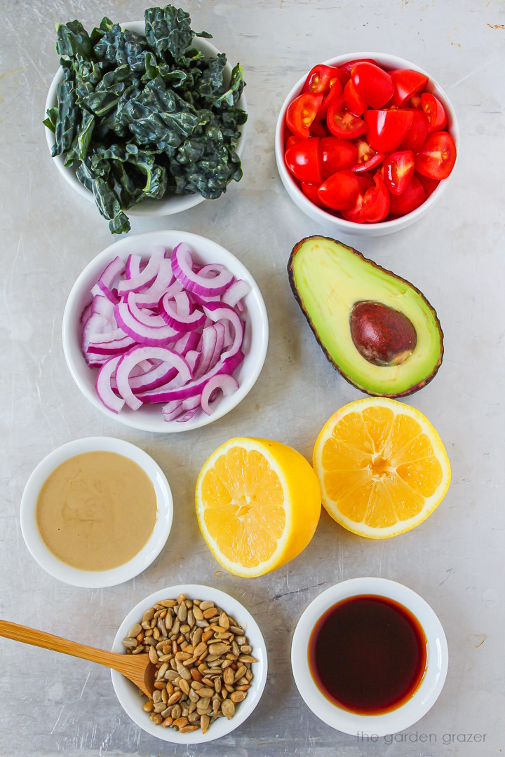 Fresh greens, tomatoes, red onion, avocado, lemon, tahini, and tamari ingredients laid out on a metal tray