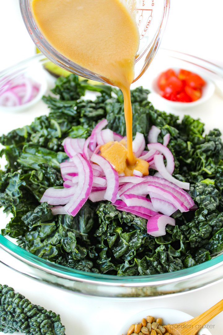 Dressing being poured over a fresh kale salad before marinating