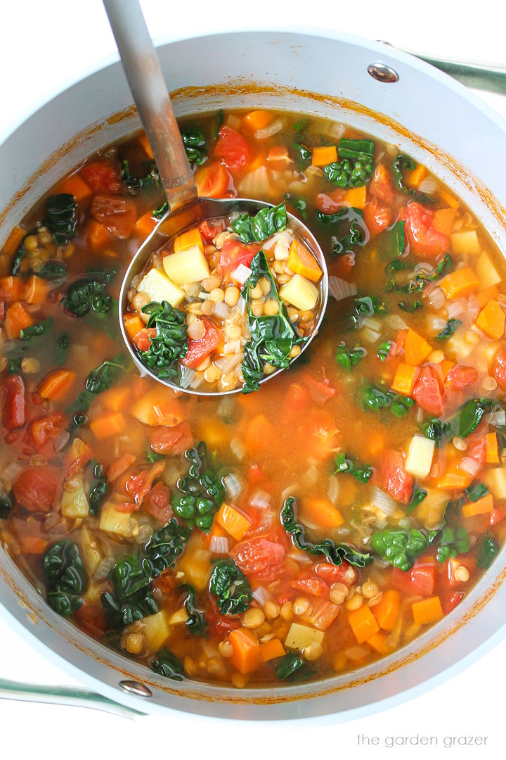 Overhead view of a ladle lifting up lentil kale potato soup as it's cooking in a pot
