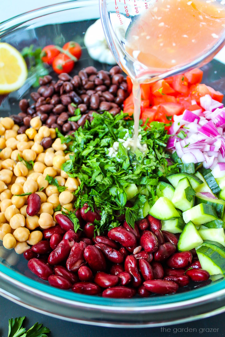 Lemon vinegar dressing being poured over a bean salad in a large glass bowl