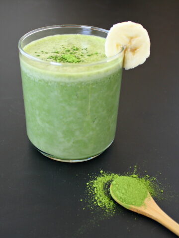 Vegan creamy banana matcha smoothie in a glass on black table
