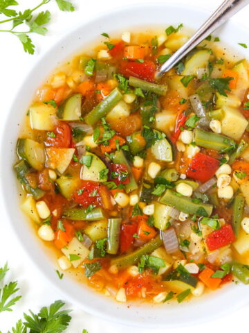 Fresh vegan garden soup in a white bowl with spoon