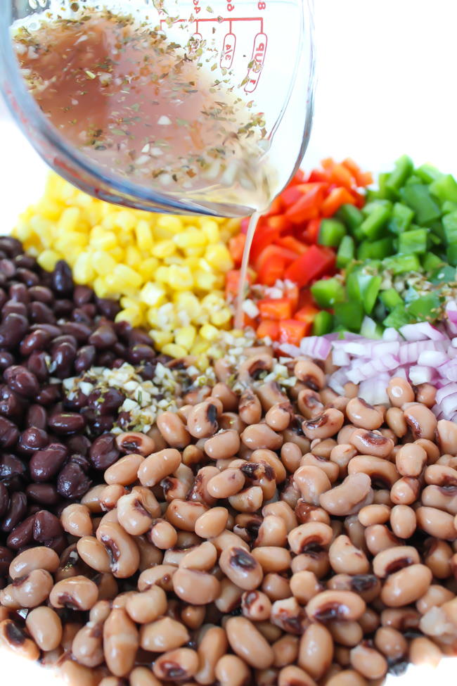 Ingredients for Texas Caviar in a bowl with dressing being poured on top