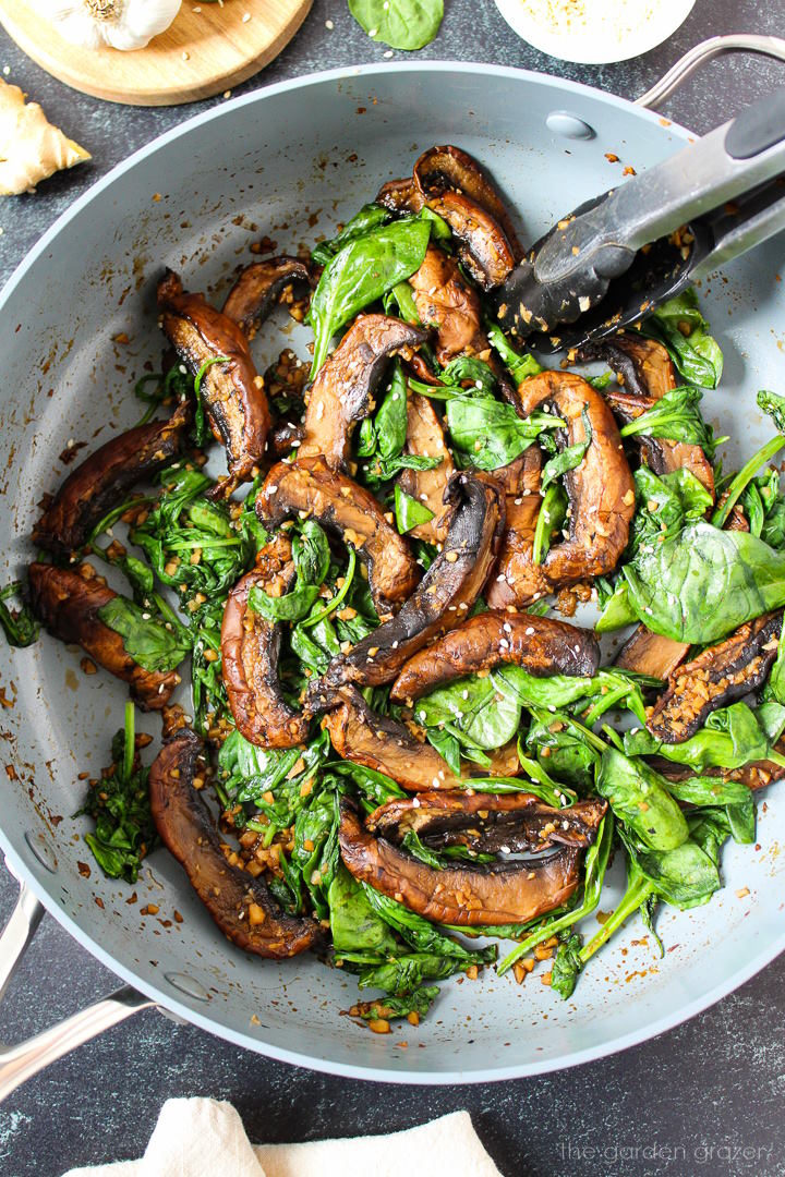 Sauteed spinach and Portobello mushrooms cooking in a large skillet with tongs