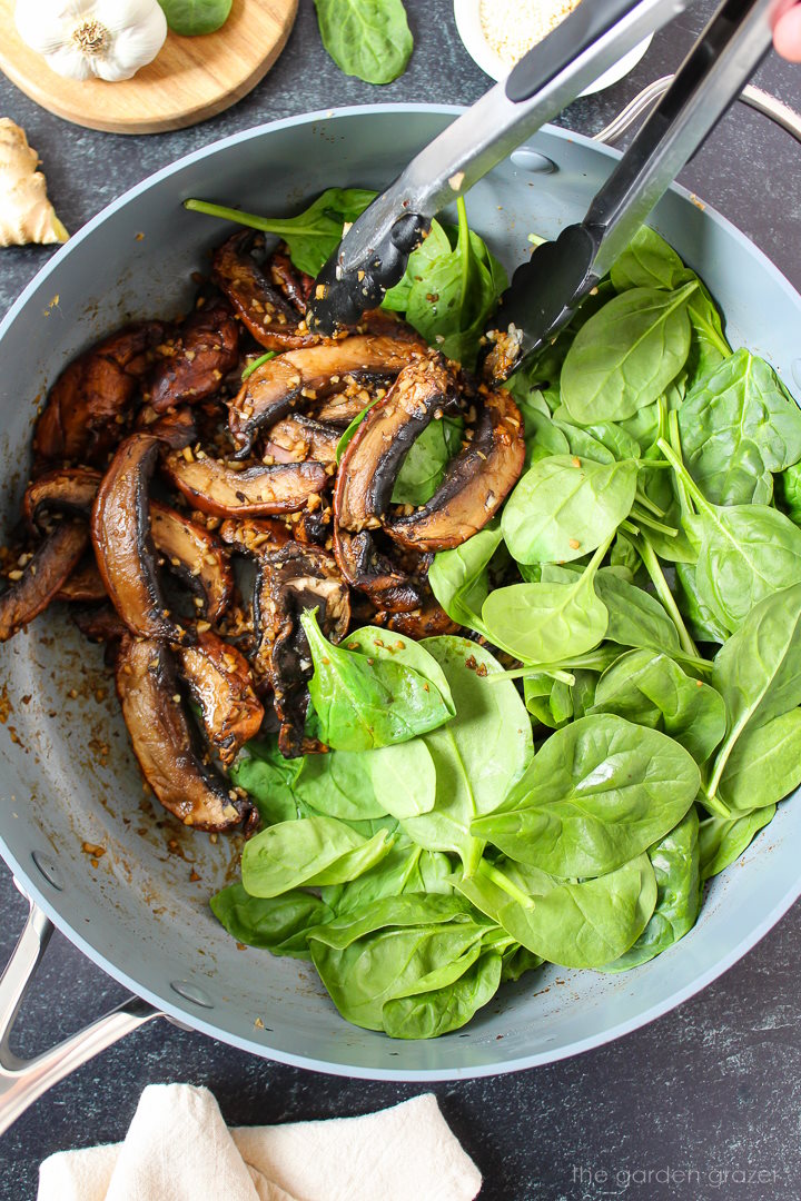 Overhead view of preparing sauteed spinach and mushrooms in a skillet
