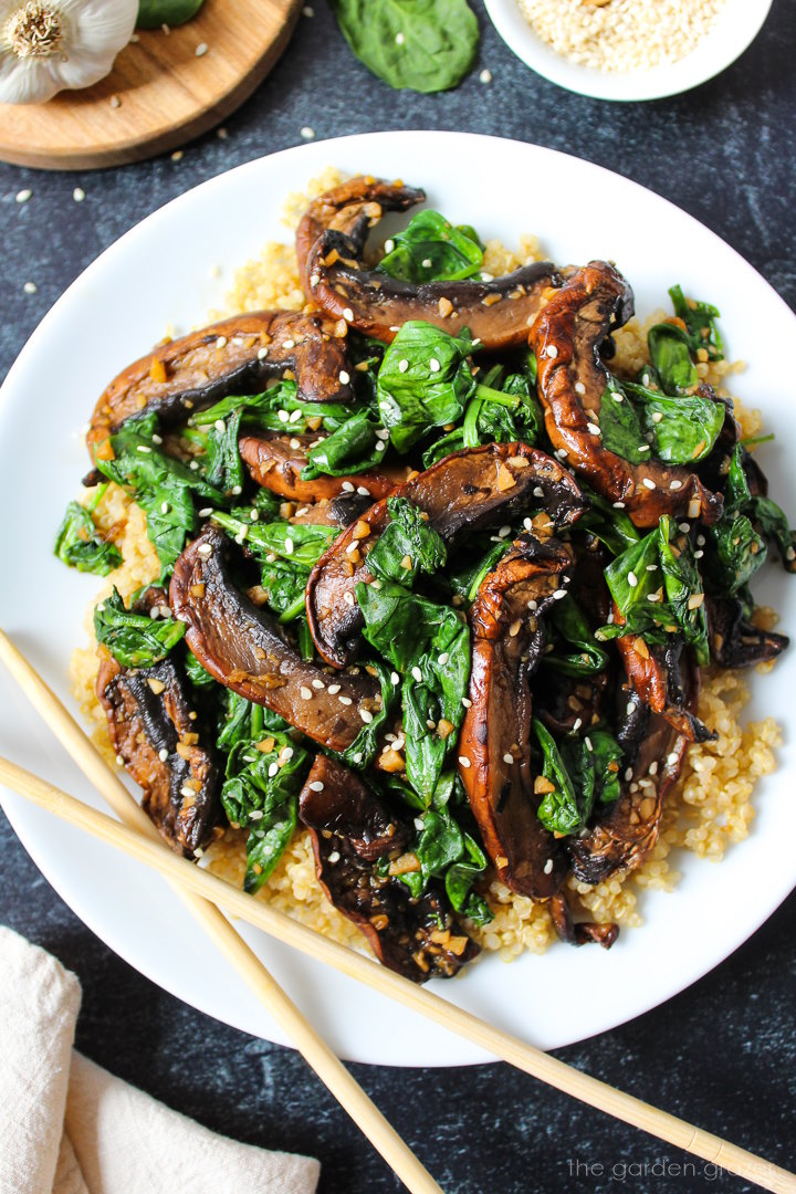 Sauteed spinach and Portobello mushrooms topped with sesame seeds on a white serving plate