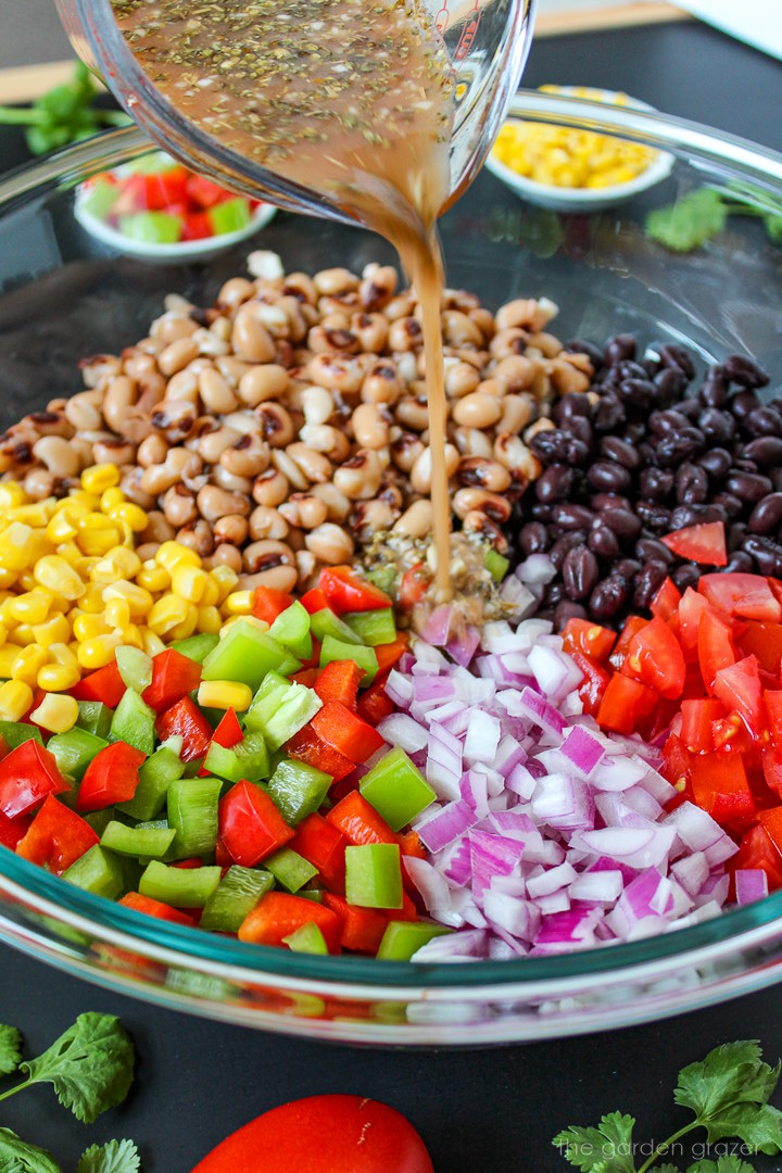 Vinegar dressing being poured over vegan cowboy caviar in a large glass bowl