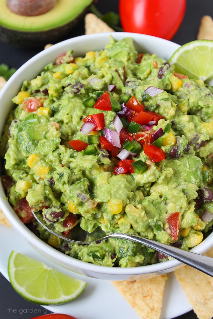 Close up view of loaded black bean guacamole in a white bowl with serving spoon