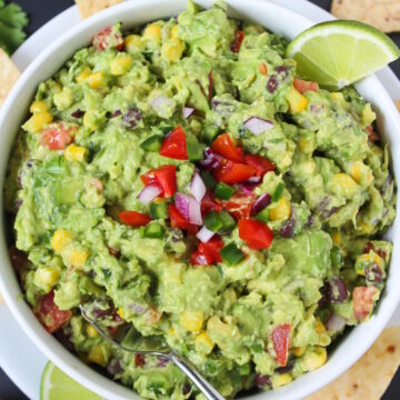 Overhead view of loaded guacamole with black beans and corn in a white bowl with lime slice