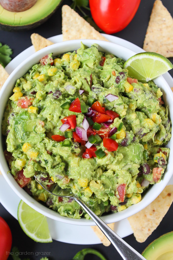 Overhead view of loaded guacamole with black beans and corn in a white bowl with lime slice