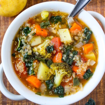 Quinoa potato soup in a white serving bowl with spoon on a wooden table